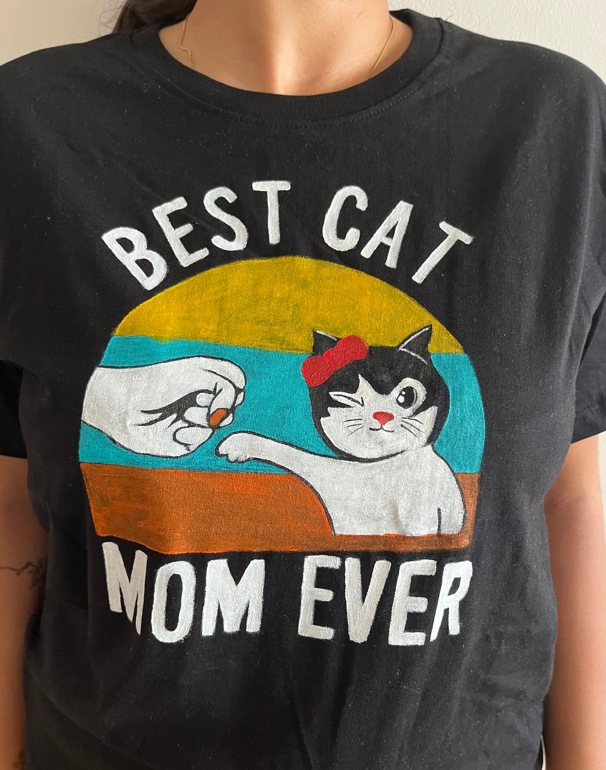 Close-up of a unique hand-painted cat mom t-shirt design, showing a cute cat giving a fist bump with "BEST CAT MOM EVER" text.