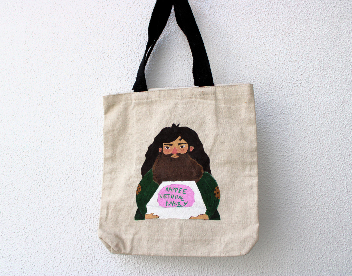 Full view of a unique hand-painted Hagrid Harry Potter cake tote bag on natural canvas, featuring Hagrid holding the "Happee Birthdae Harry" cake.