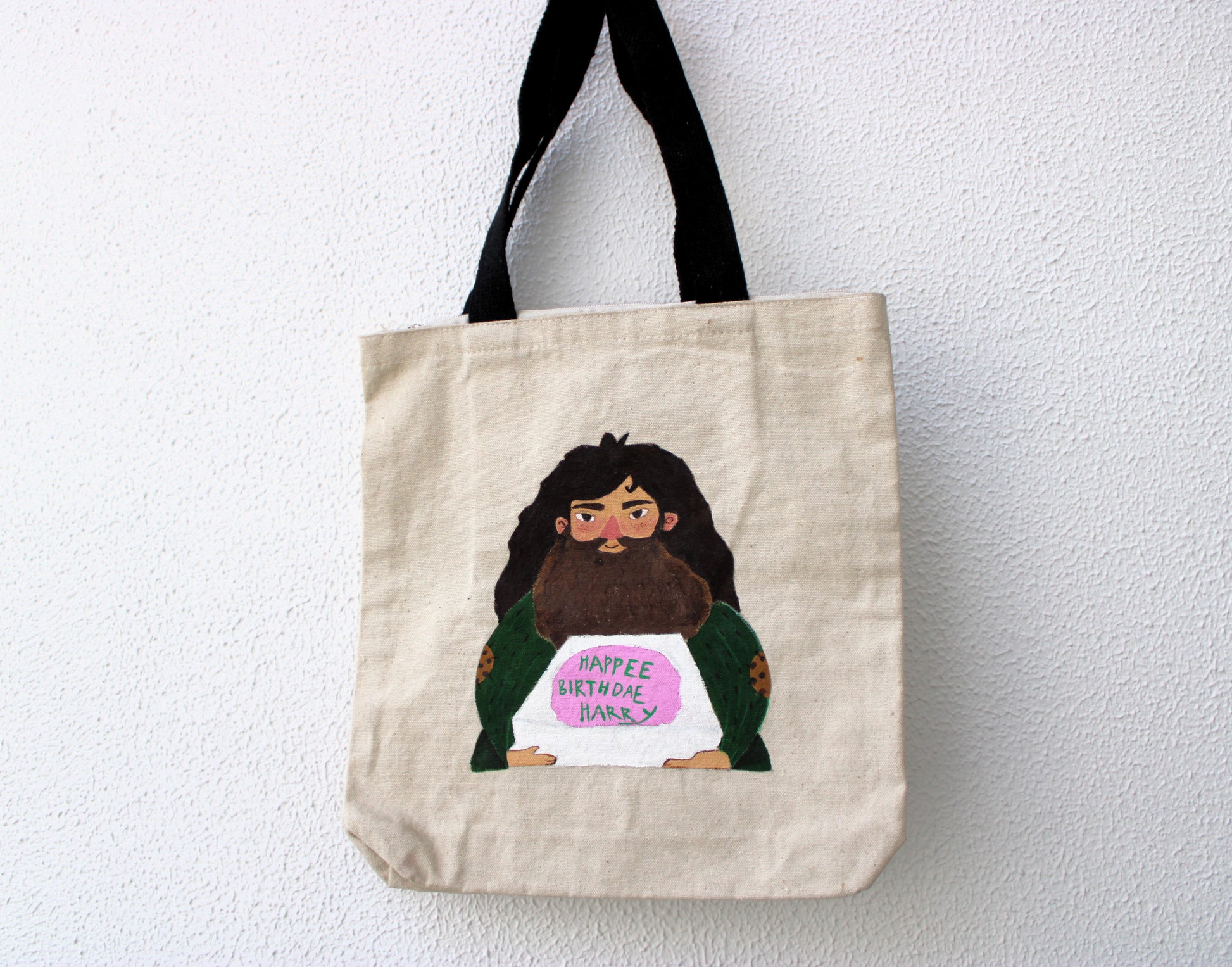 Full view of a unique hand-painted Hagrid Harry Potter cake tote bag on natural canvas, featuring Hagrid holding the "Happee Birthdae Harry" cake.