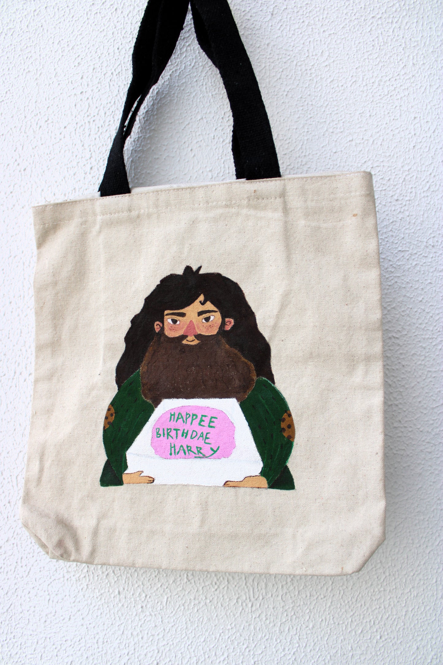 Close-up of the detailed hand-painted Harry Potter birthday cake Hagrid design on the tote bag, showing the cake and text.
