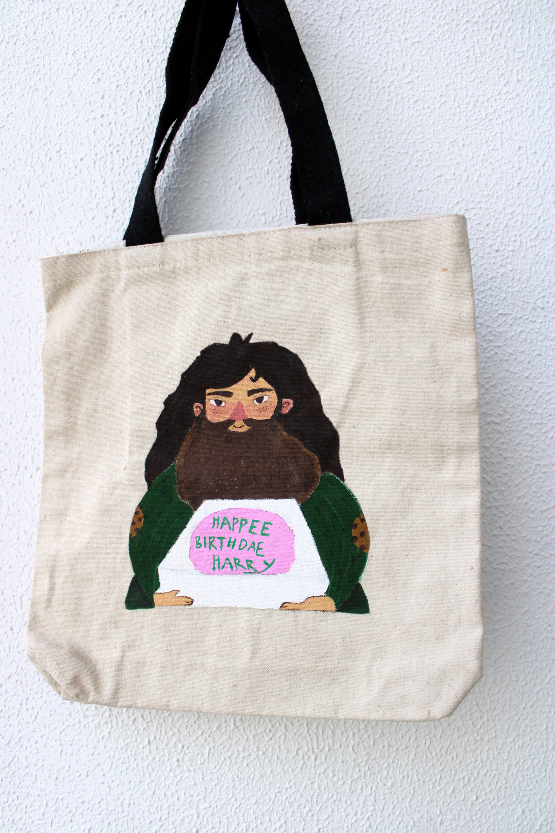 Close-up of the detailed hand-painted Harry Potter birthday cake Hagrid design on the tote bag, showing the cake and text.