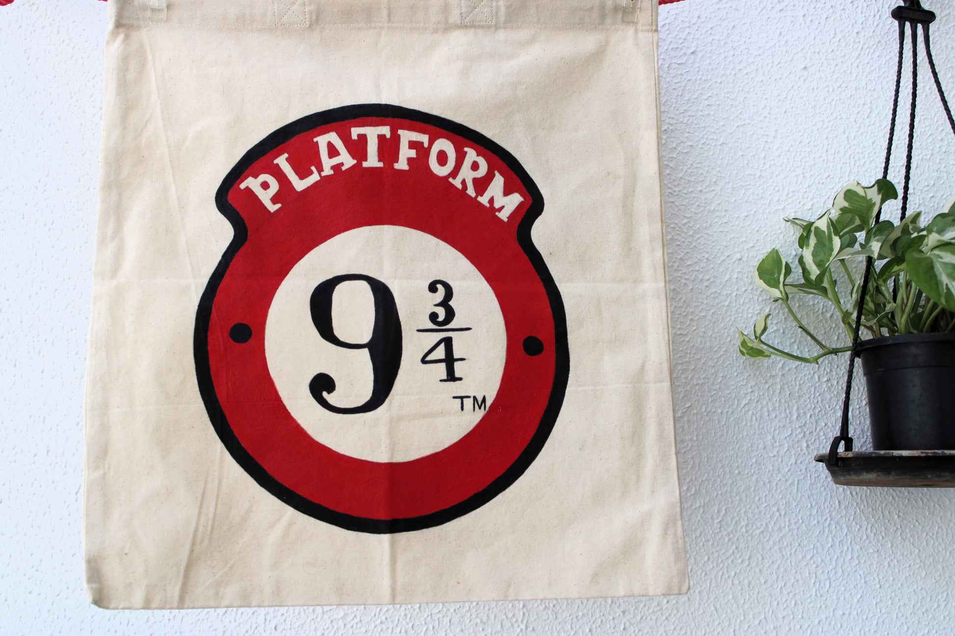Full view of a unique hand-painted Platform 9 3/4 tote bag on natural canvas, featuring the iconic red and black Harry Potter logo.