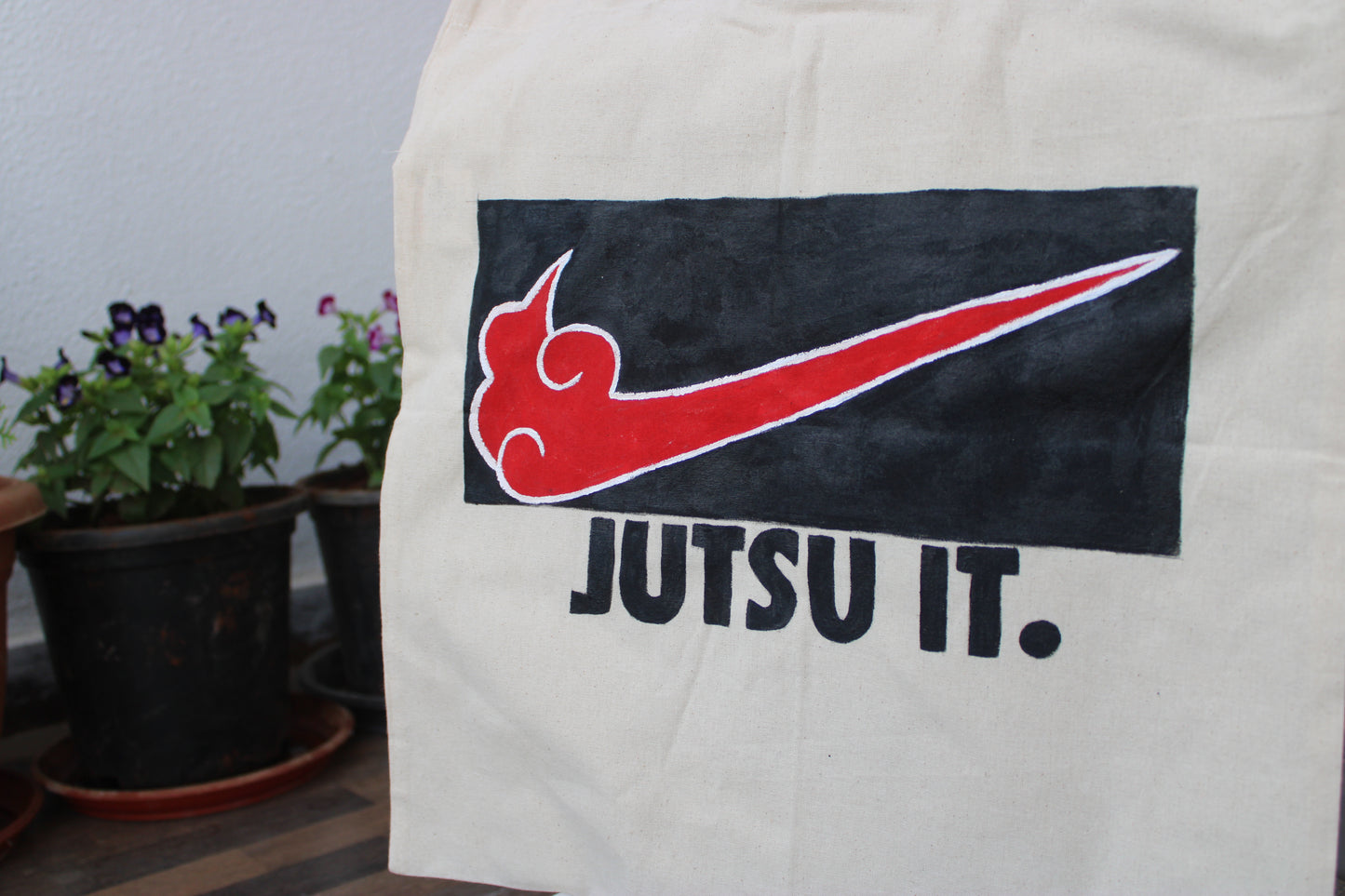 Front view of a unique hand-painted "Jutsu It" tote bag on natural canvas, featuring an Akatsuki-style swoosh and bold text.