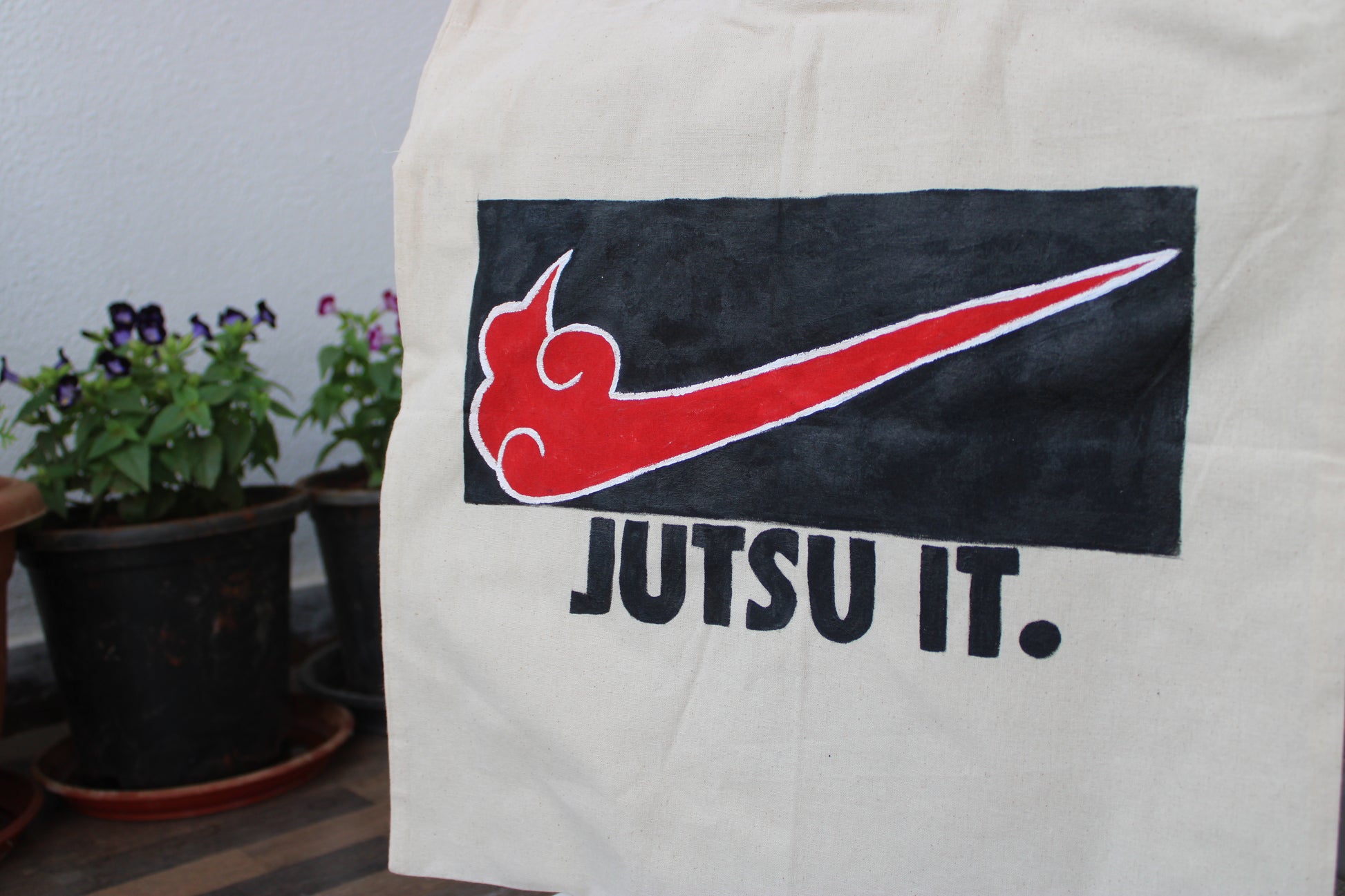Front view of a unique hand-painted "Jutsu It" tote bag on natural canvas, featuring an Akatsuki-style swoosh and bold text.