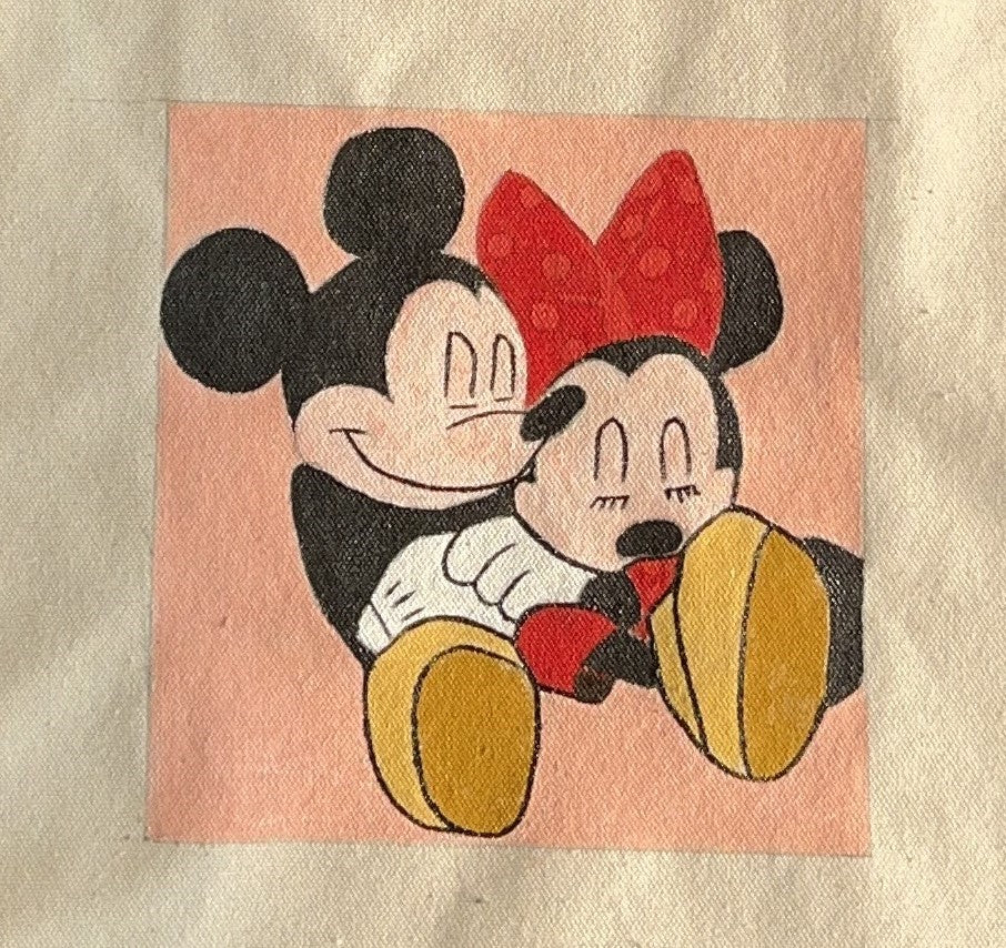 A hand-painted tote bag featuring Mickey Mouse and Minnie Mouse in a vibrant, cheerful poses on a beige background.